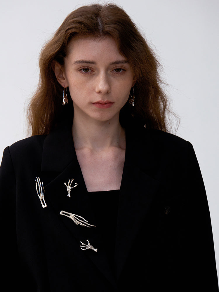 Woman wearing a black blazer with white embroidered designs on a plain background