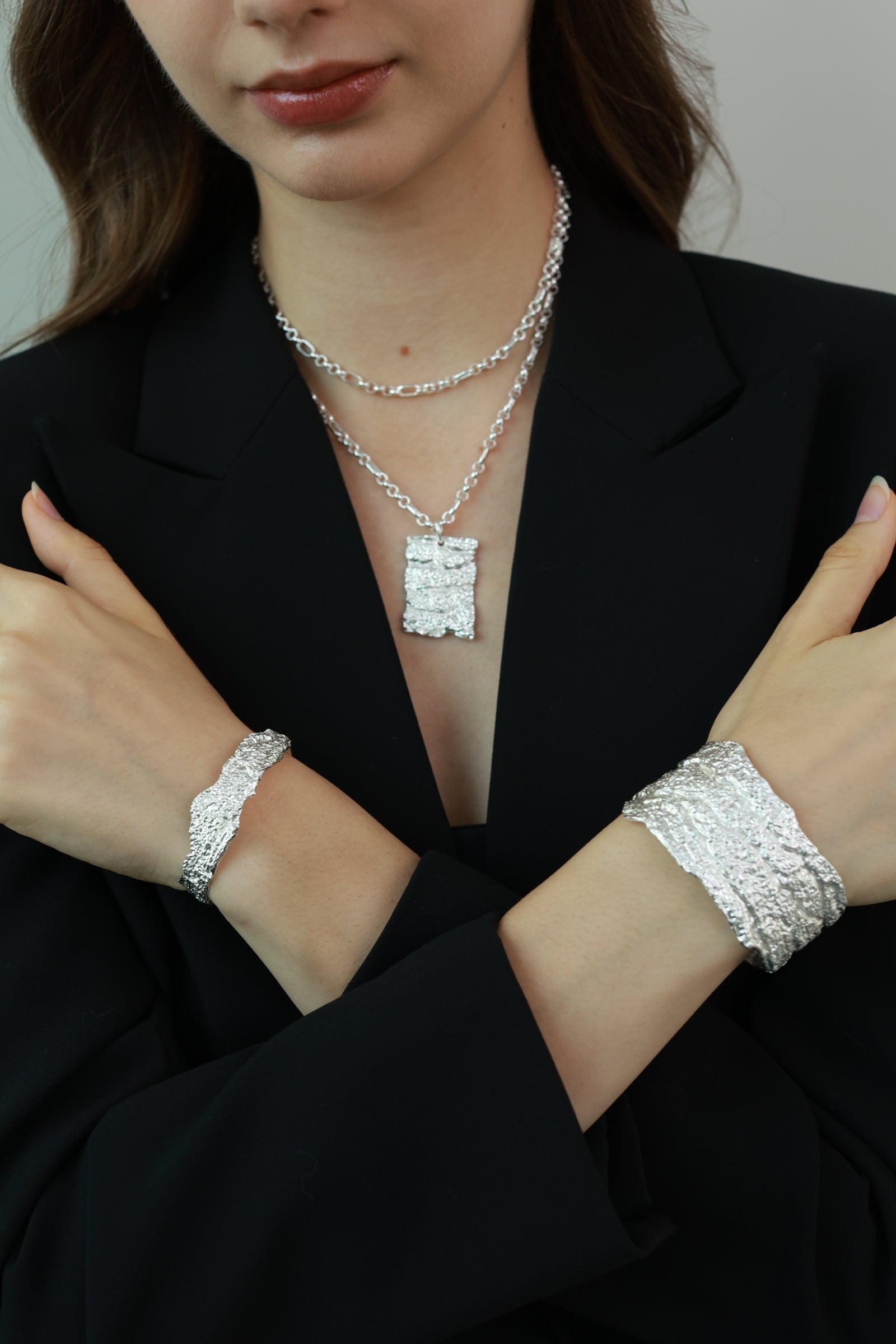 Woman wearing silver jewelry including a bracelet and necklace against a black background