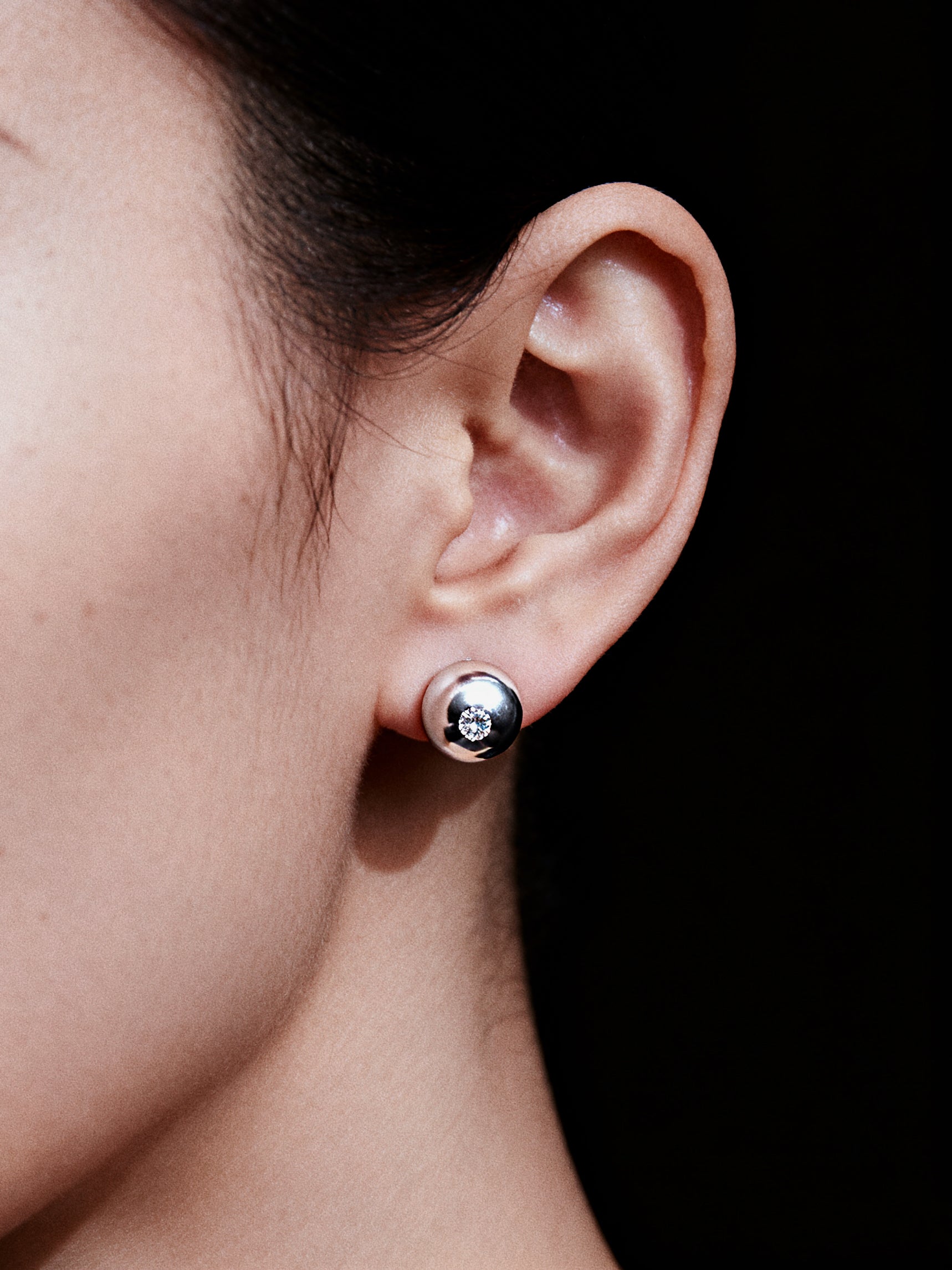Close-up of an ear wearing a silver earring with a clear gemstone on a black background