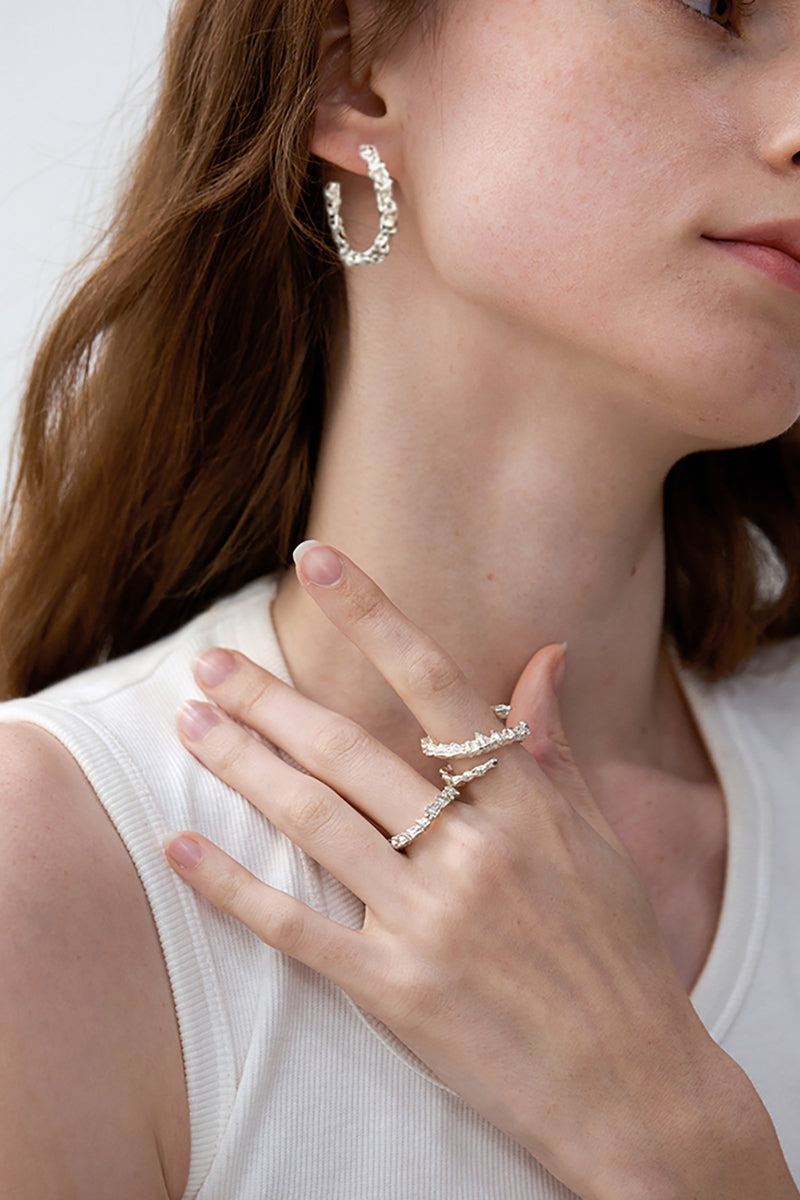 Amazon · Double Coil Snakebone Silver Ring — Close-up of a woman wearing silver hoop earrings and rings on a plain background
