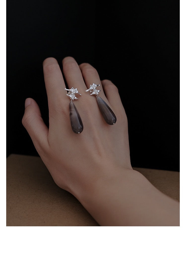Amazon · Spine & Quartz Raindrop Earrings — Hand wearing a ring with a teardrop-shaped gemstone and star design on a dark