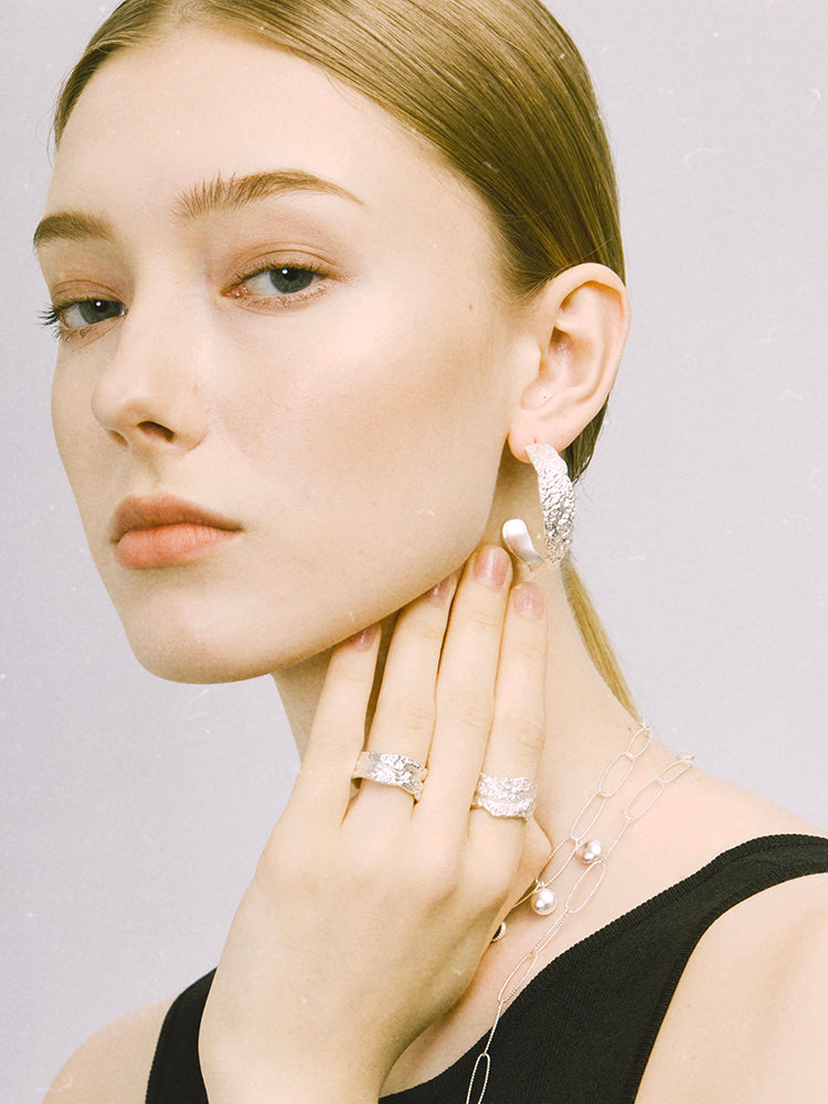 Amazon · Tree Grain Hoop Earrings — Woman wearing diamond earrings and rings on a plain background