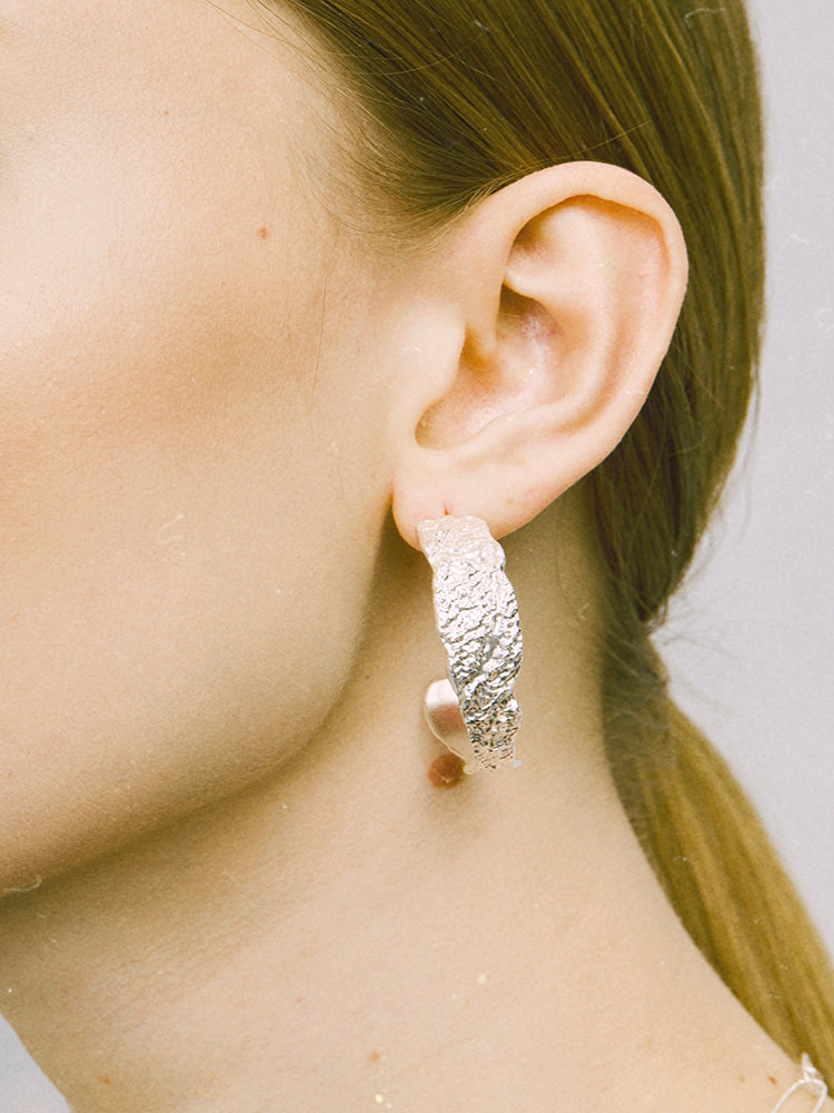 Amazon · Tree Grain Hoop Earrings — Close-up of a person wearing a textured silver earring with a pearl accent.