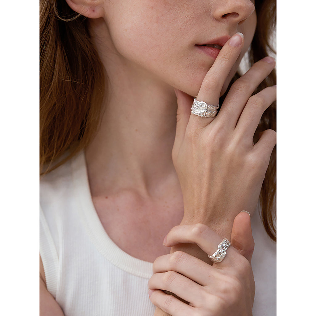 Amazon · Tree Grain Wide Band Silver Ring — Close-up of a woman's hand wearing a silver ring with a white background
