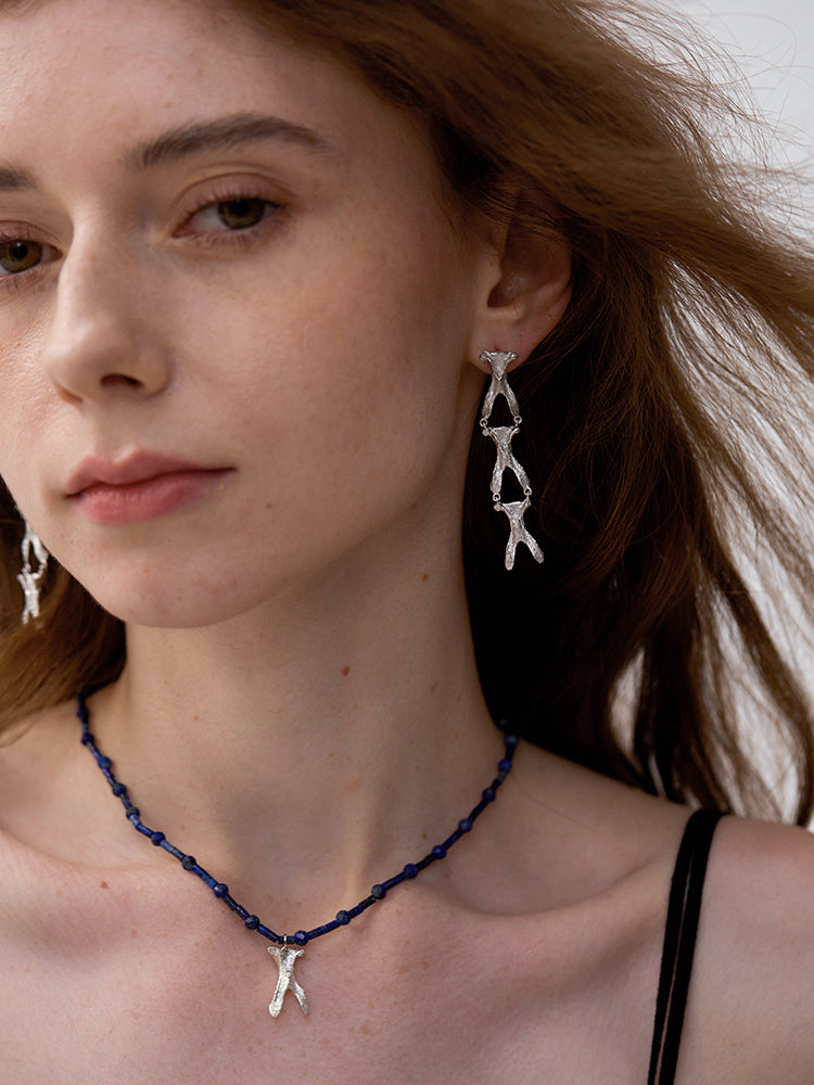 Amazon Wishbone — Woman wearing silver earrings and a necklace with a blue cord
