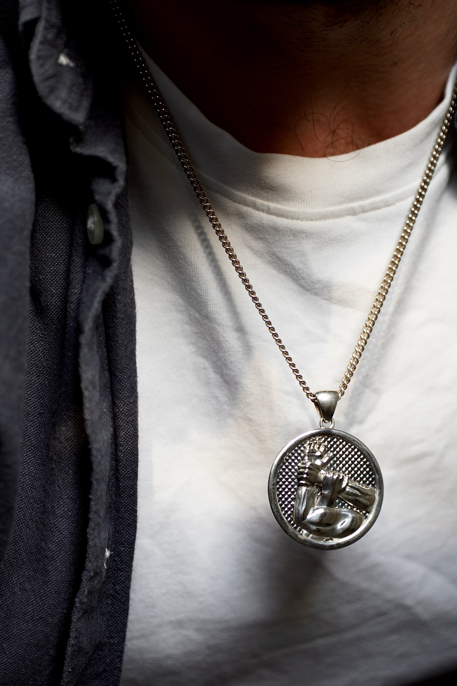 Close-up of a person wearing a necklace with a pendant on a white shirt.