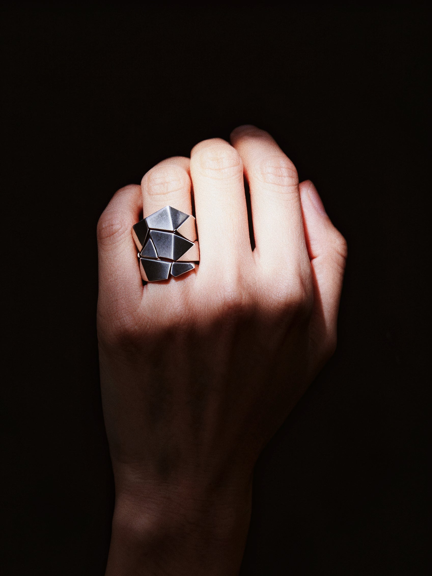 Hand wearing a geometric ring against a dark background