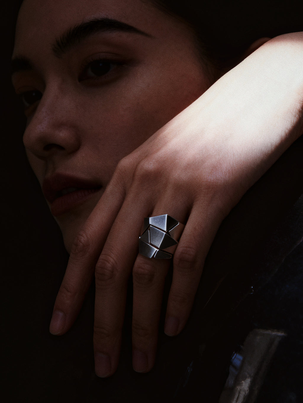 Close-up of a hand wearing a geometric silver ring with a dark background