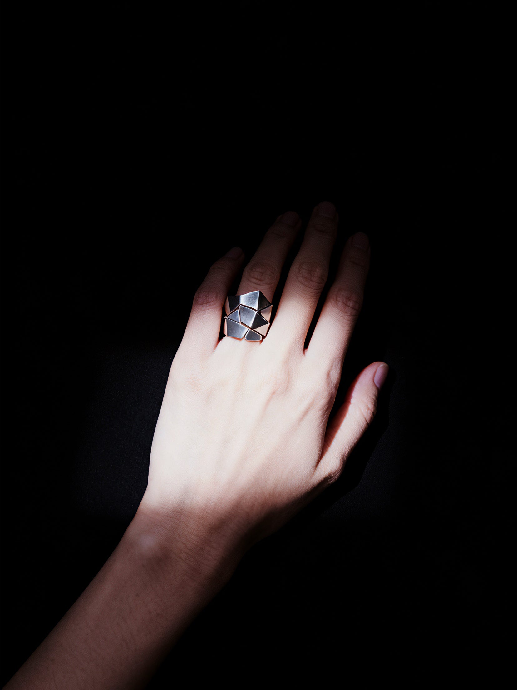 Hand wearing a large, faceted ring against a dark background