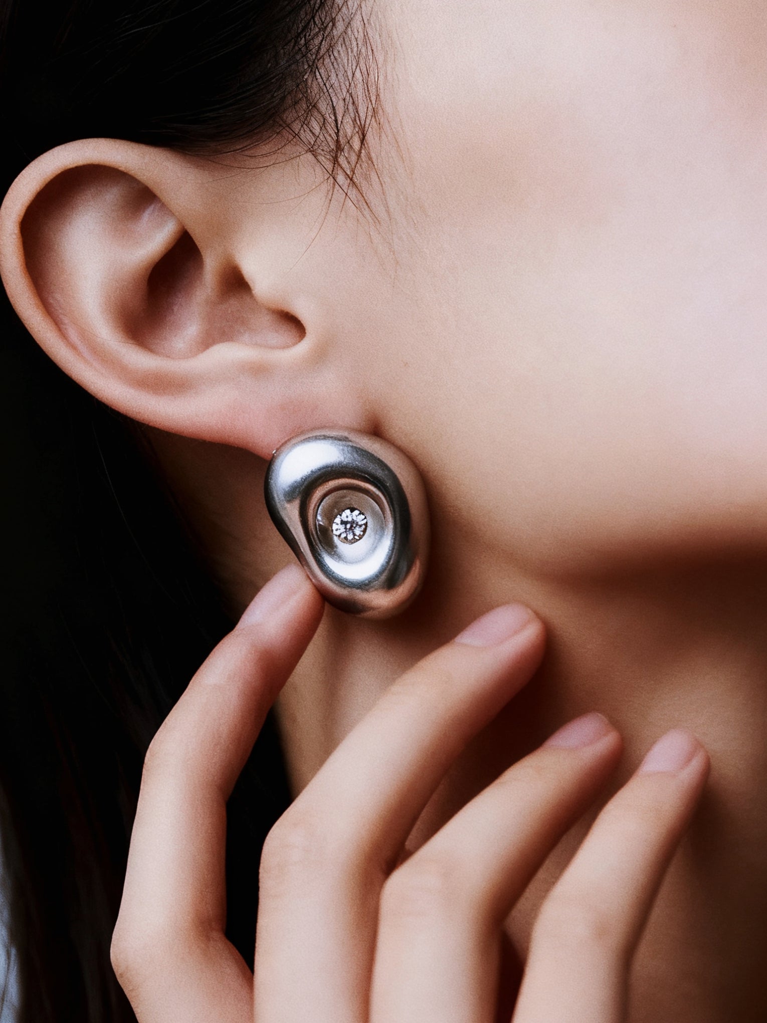 Close-up of a person wearing a silver earring with a clear gemstone.