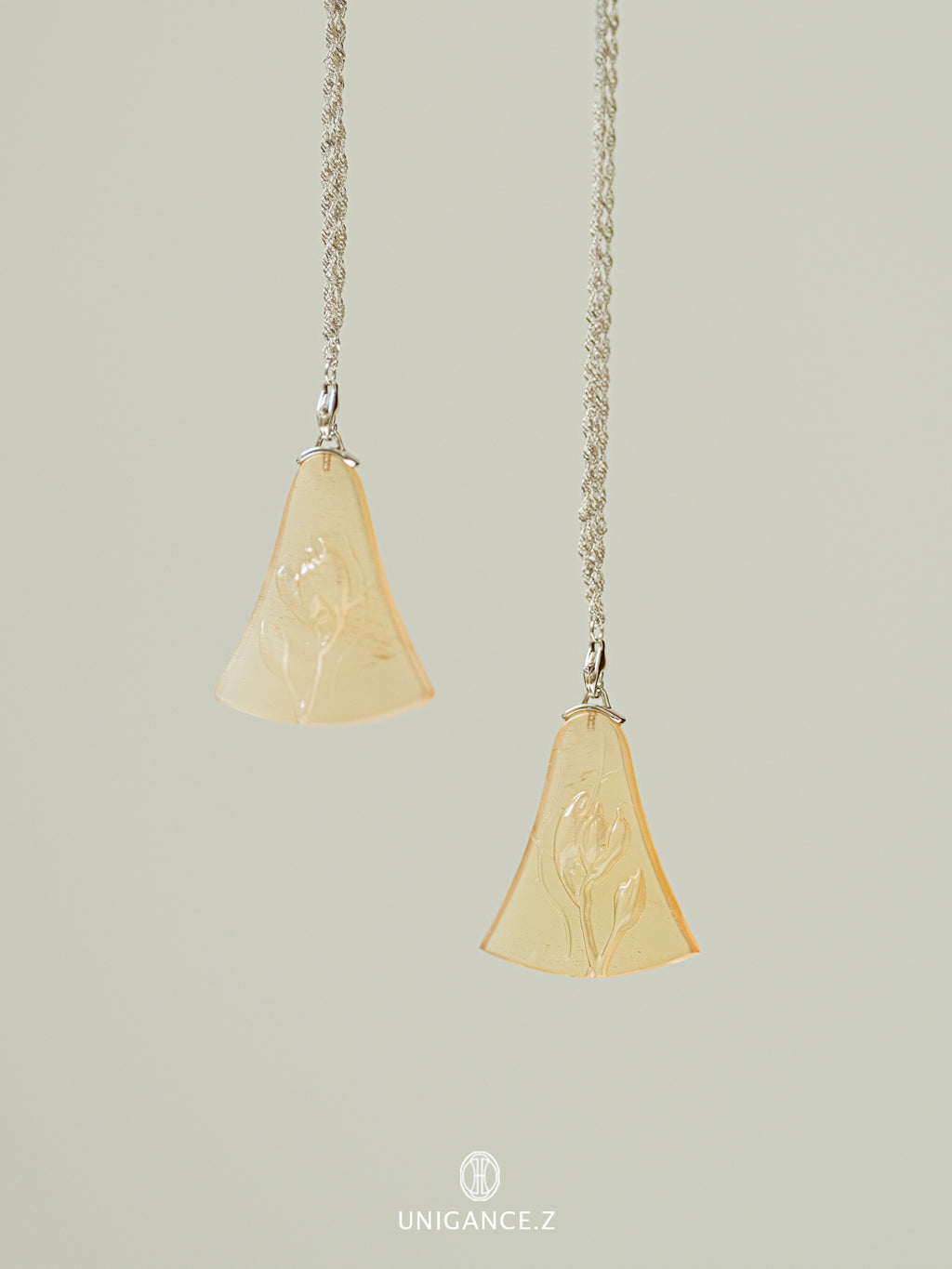 Two pendant necklaces with beige stone pendants on a light gray background.