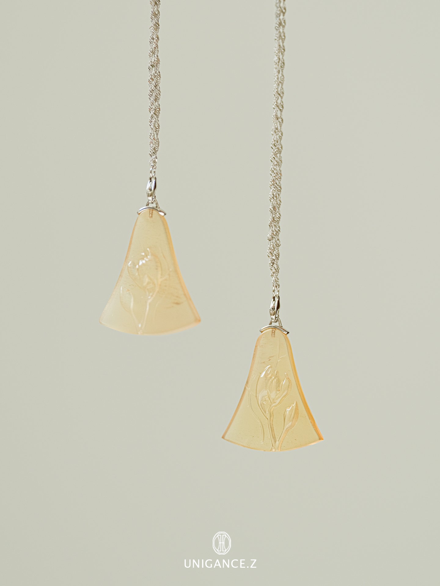 Two pendant necklaces with beige stone pendants on a light gray background.