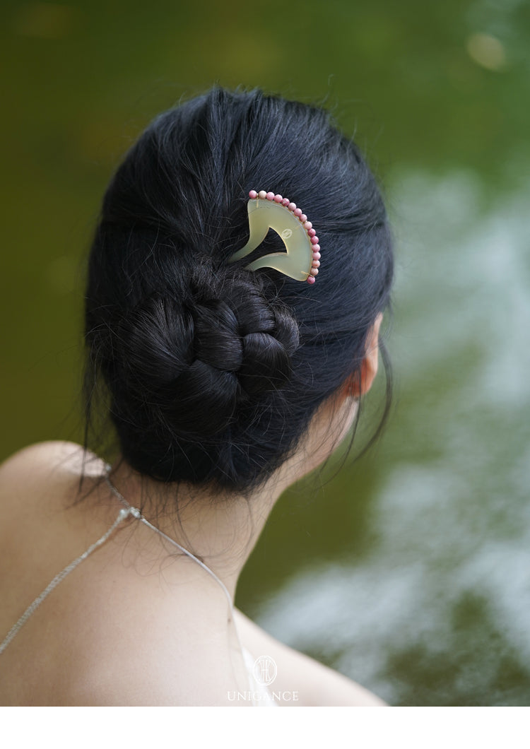 Person with intricately styled hair featuring a decorative hairpin against a blurred natural background