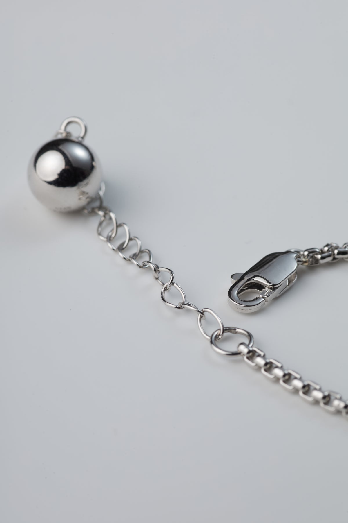 Asymmetric Heart Necklace — Silver bracelet with a spherical charm on a light gray background