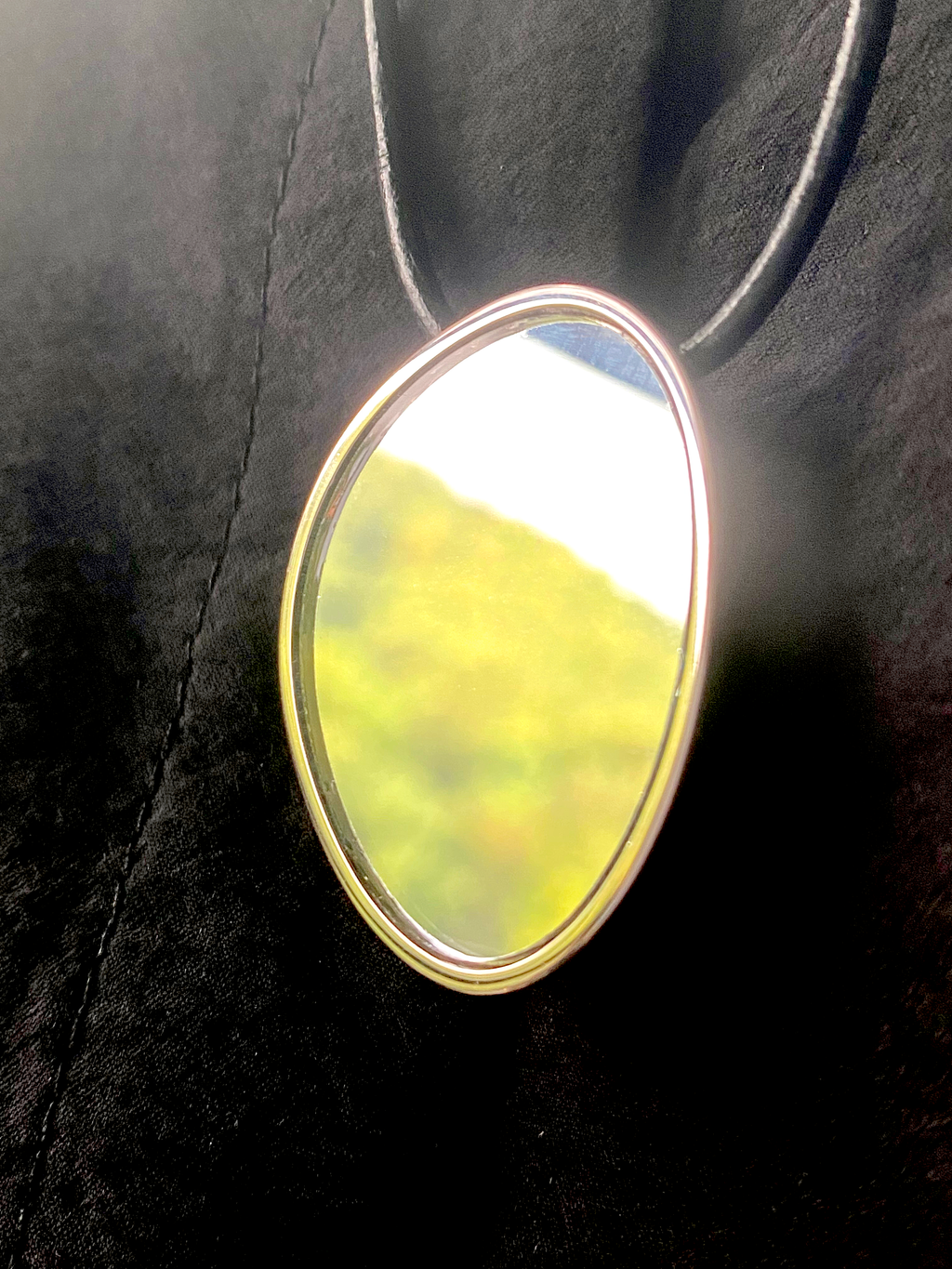 Avocado Mirror Pendant Necklace — Round mirror with a yellow reflection on a dark textured surface