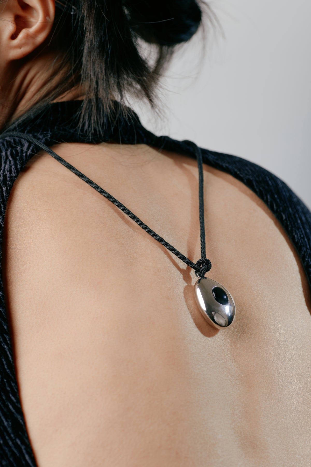 Avocado Mirror Pendant Necklace — Necklace with a pendant on a person wearing a black top against a neutral background