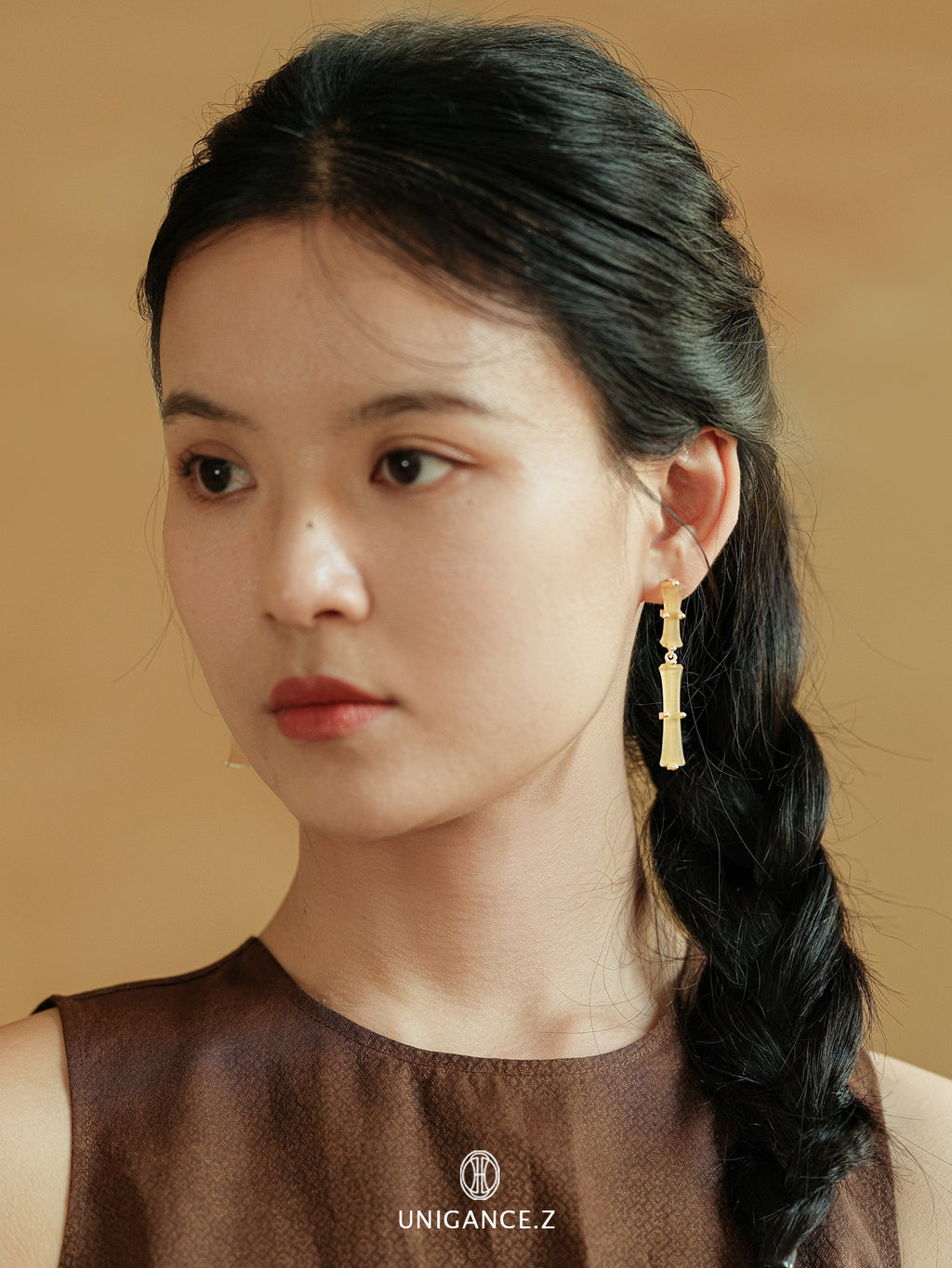 Bamboo Branch Drop Earrings — Woman with braided hair wearing gold earrings against a beige background