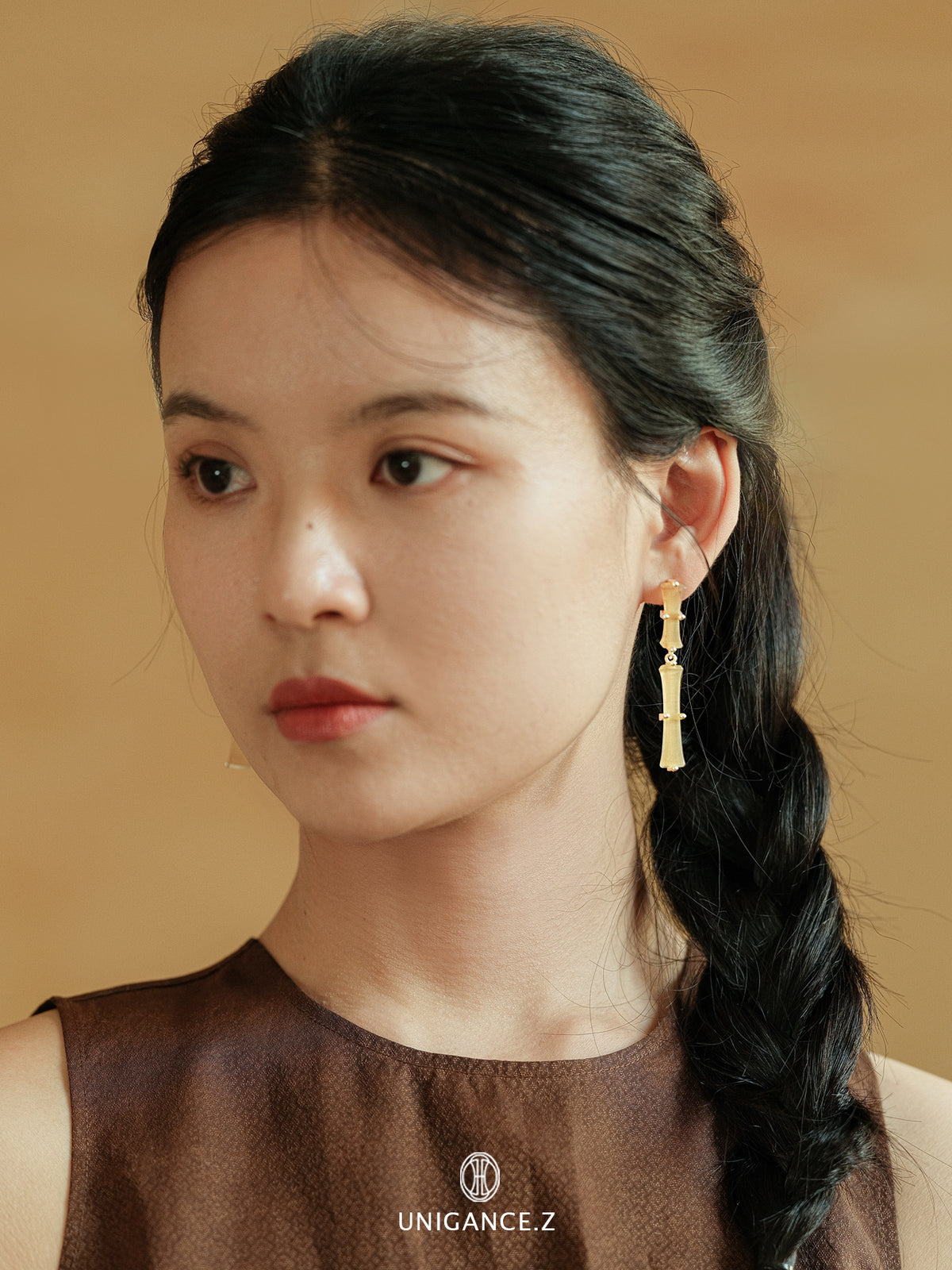 Bamboo Branch Drop Earrings — Woman with braided hair wearing gold earrings against a beige background