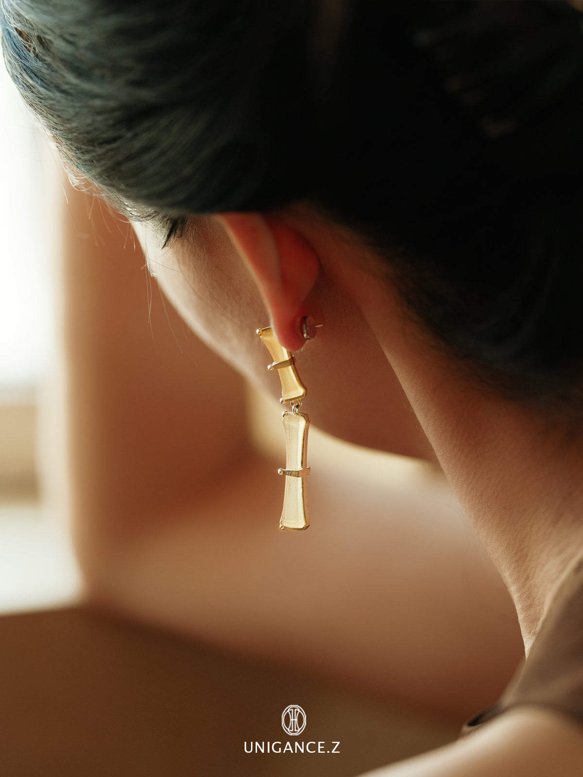 Bamboo Branch Drop Earrings — Gold earring worn by a person with blurred background