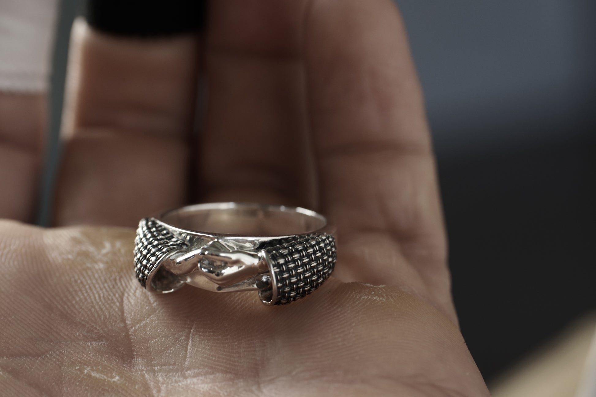 Silver ring with intricate design held in a hand against a blurred background