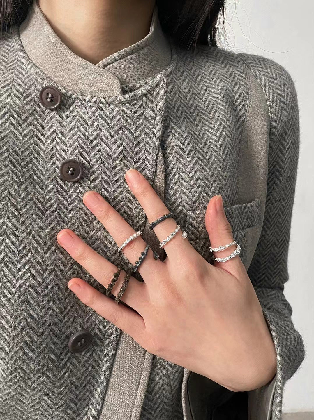Person wearing a gray herringbone coat with a close-up of their hand showing multiple rings.