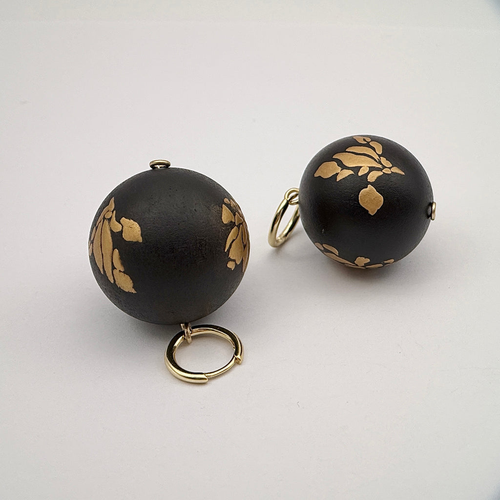 Bloom and Fade Magnolia Lacquer Quasi-Maki-e Earrings — Black spherical objects with gold leaf patterns and rings on a light
