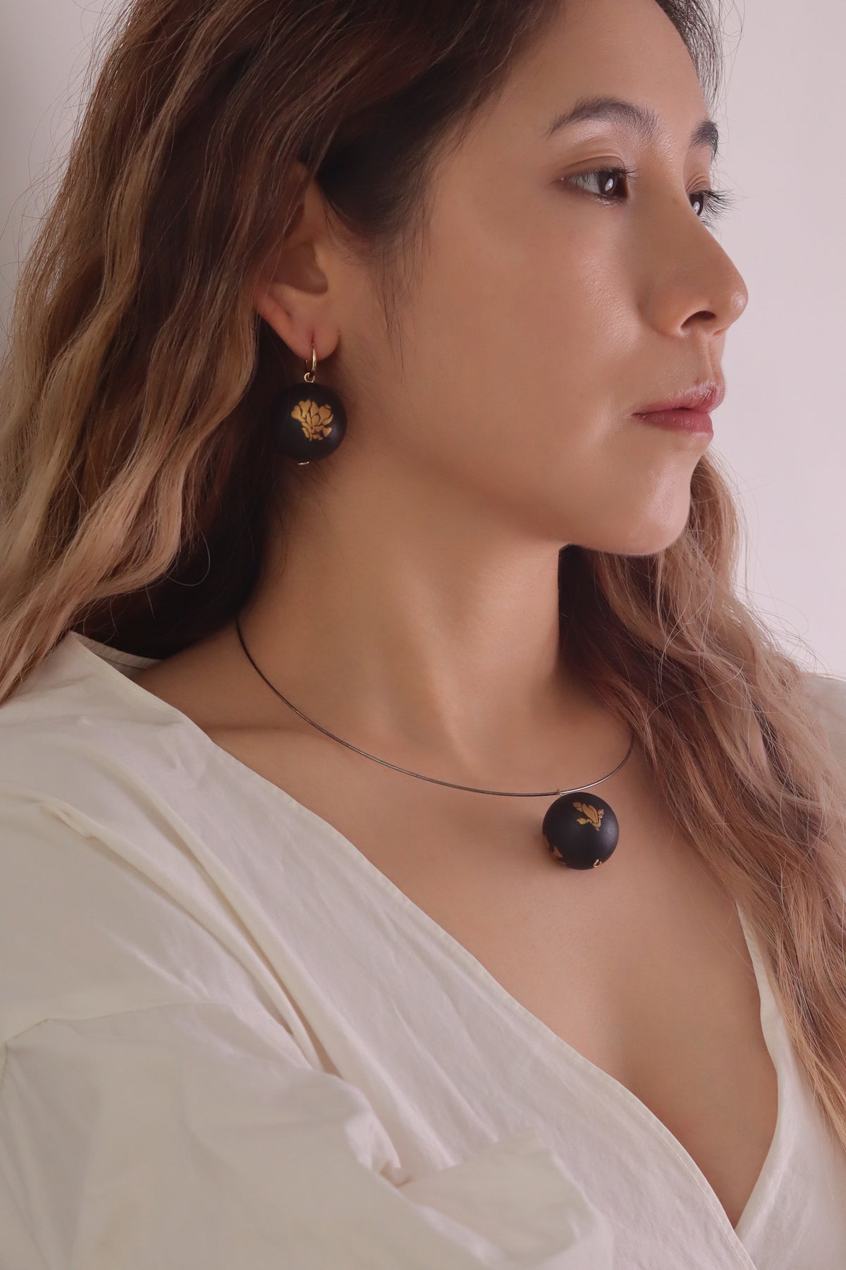 Bloom Fade Magnolia Lacquer Quasi Maki — Woman wearing a black necklace and earrings against a neutral background
