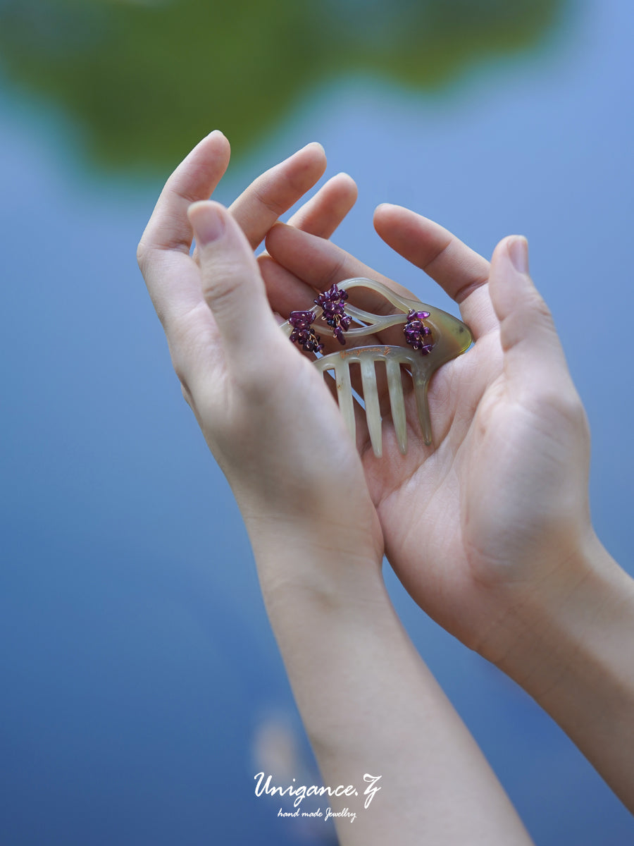 Hand holding a decorative comb with purple flowers against a blurred natural background