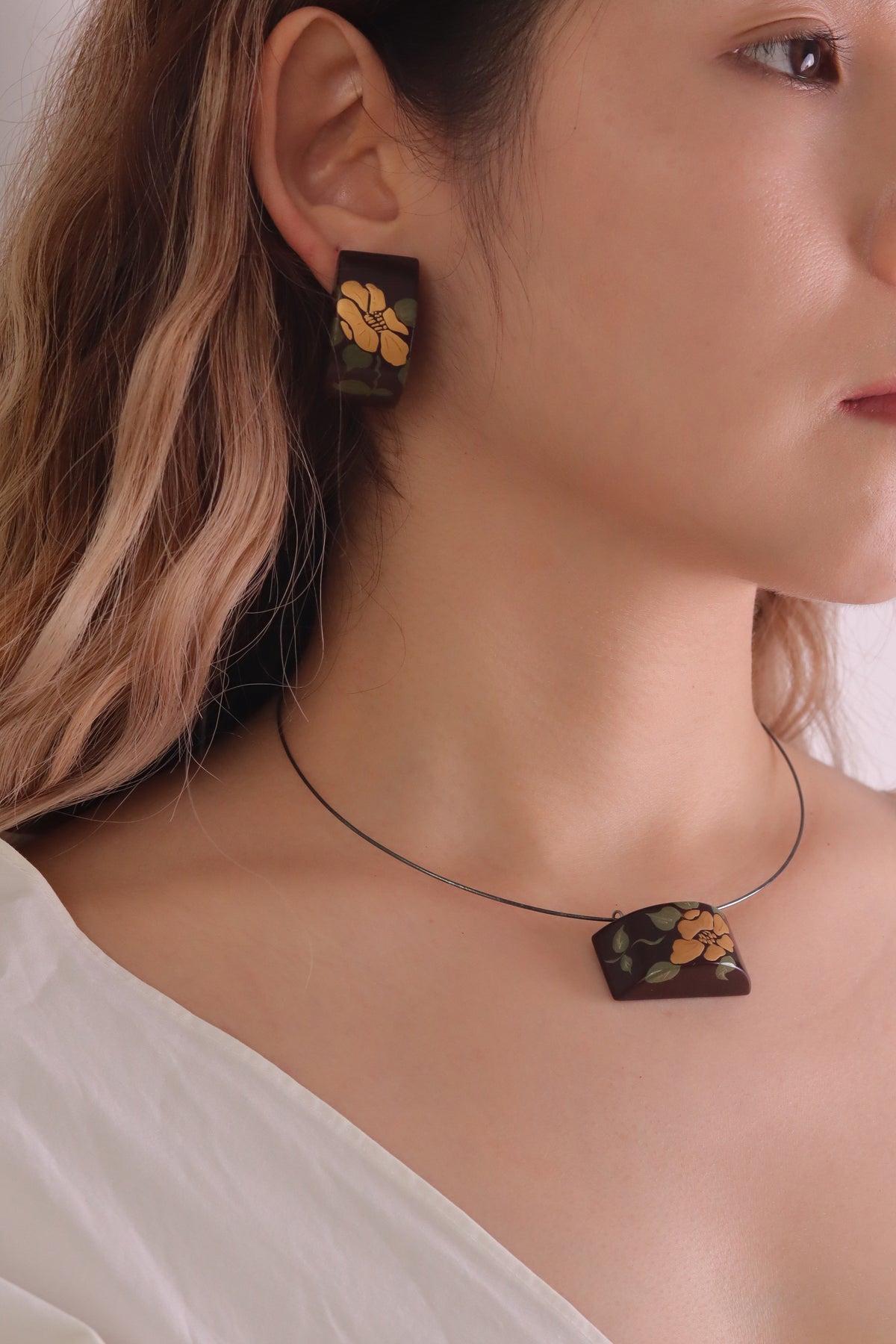 Camellia Lacquer Quasi-Maki-e Earrings — Close-up of a person wearing a necklace with floral pendant