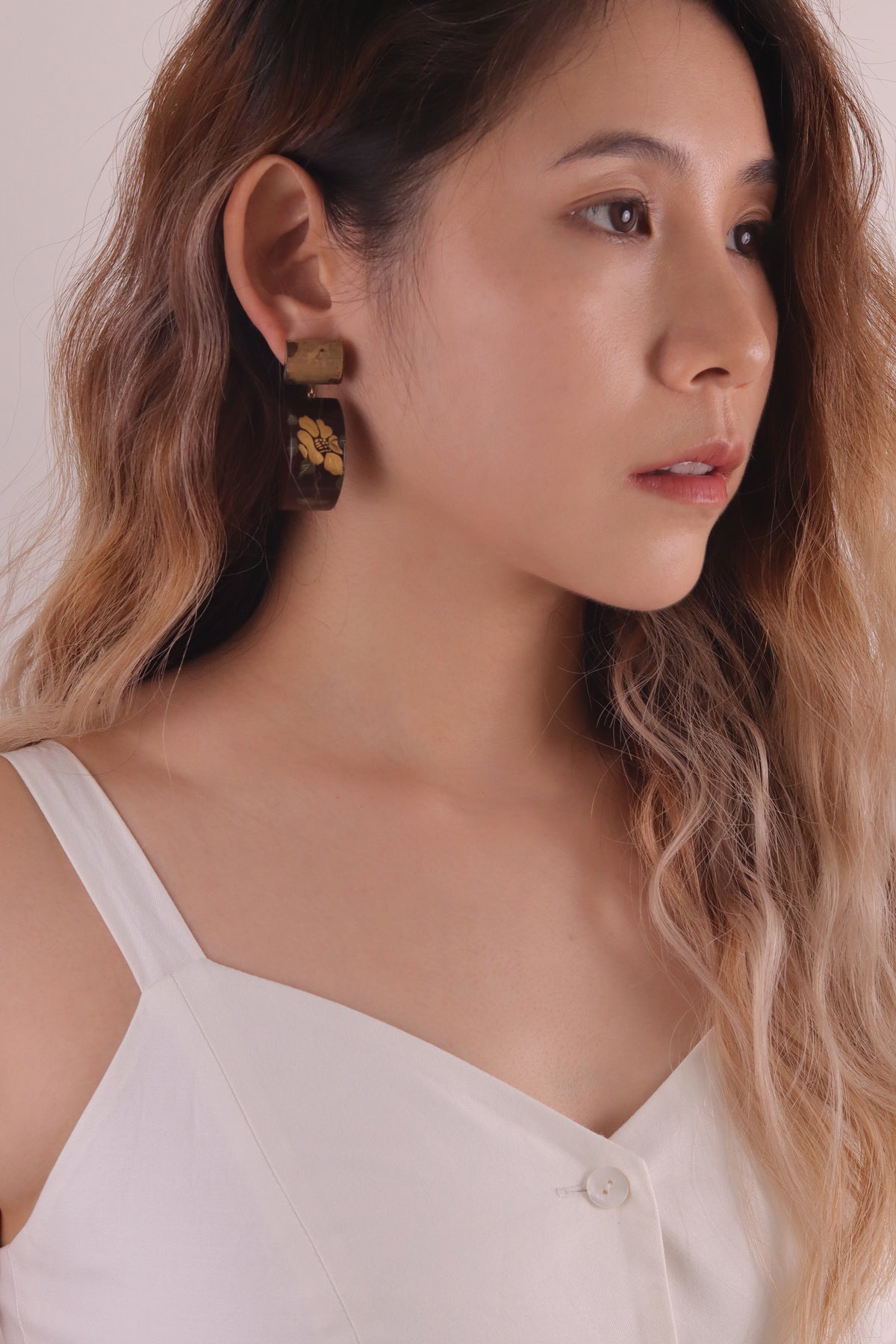 Camellia Lacquer Quasi-Maki-e Earrings — Woman wearing gold earrings with a neutral background