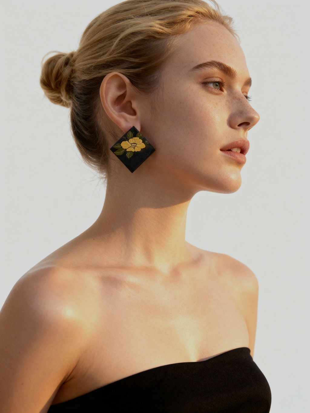 Camellia Lacquer Quasi-Maki-e Earrings — Woman wearing a black strapless top and floral earrings against a plain background