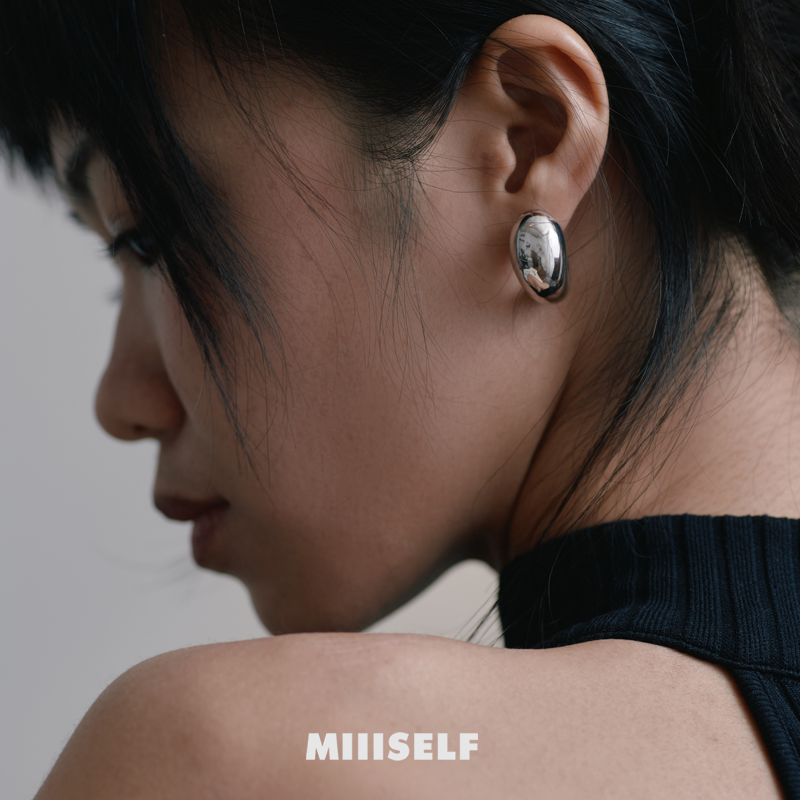 Cashew Curve Silver Earrings — Close-up of a person wearing a silver earring with 'MIISELF' branding.