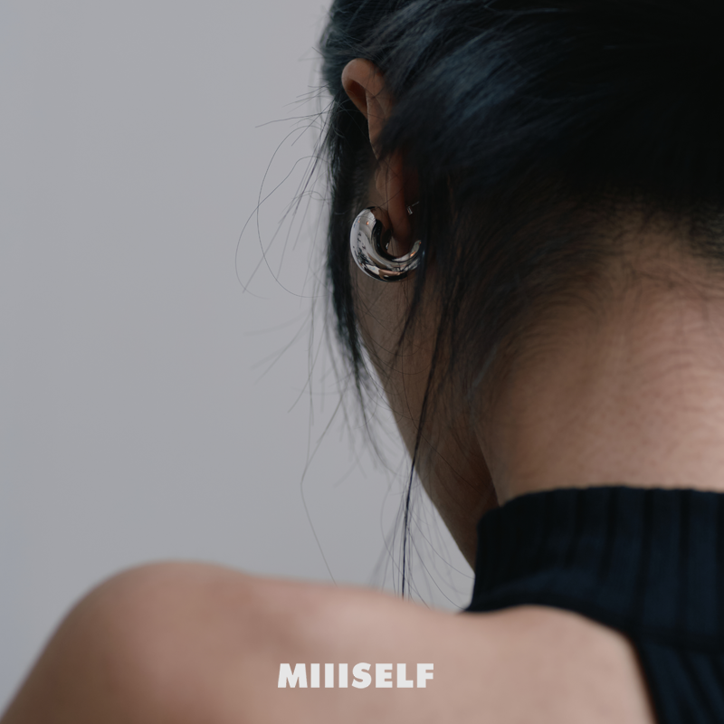 Cashew Curve Silver Earrings — Person wearing a silver hoop earring with 'MIIISELF' branding on a plain background