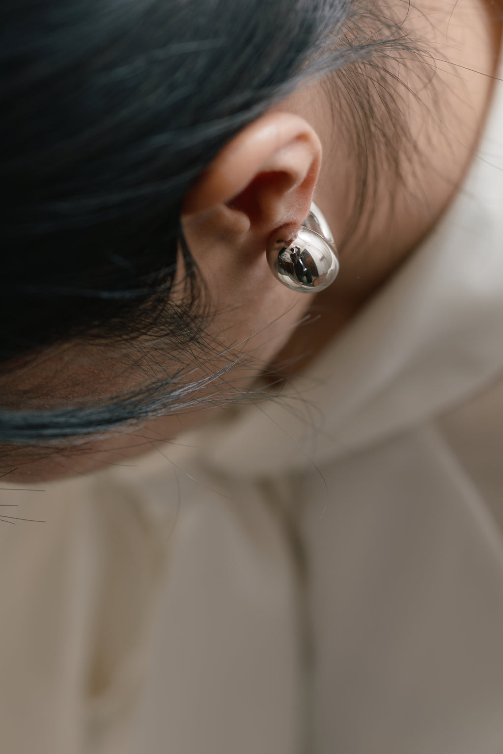 Cashew Curve Silver Earrings — Close-up of an ear wearing a silver hoop earring with a blurred background