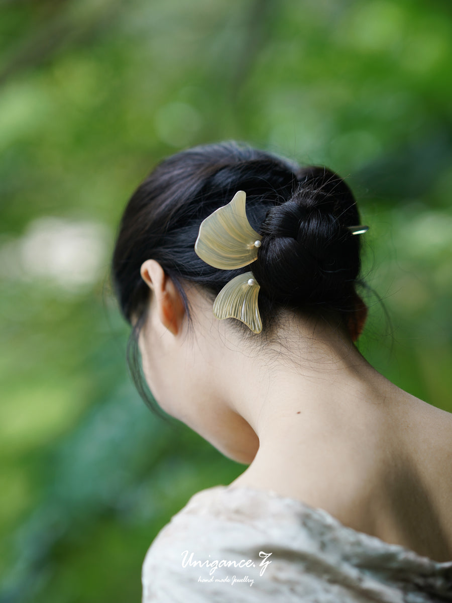 Person with a hairpin in their bun against a blurred green background