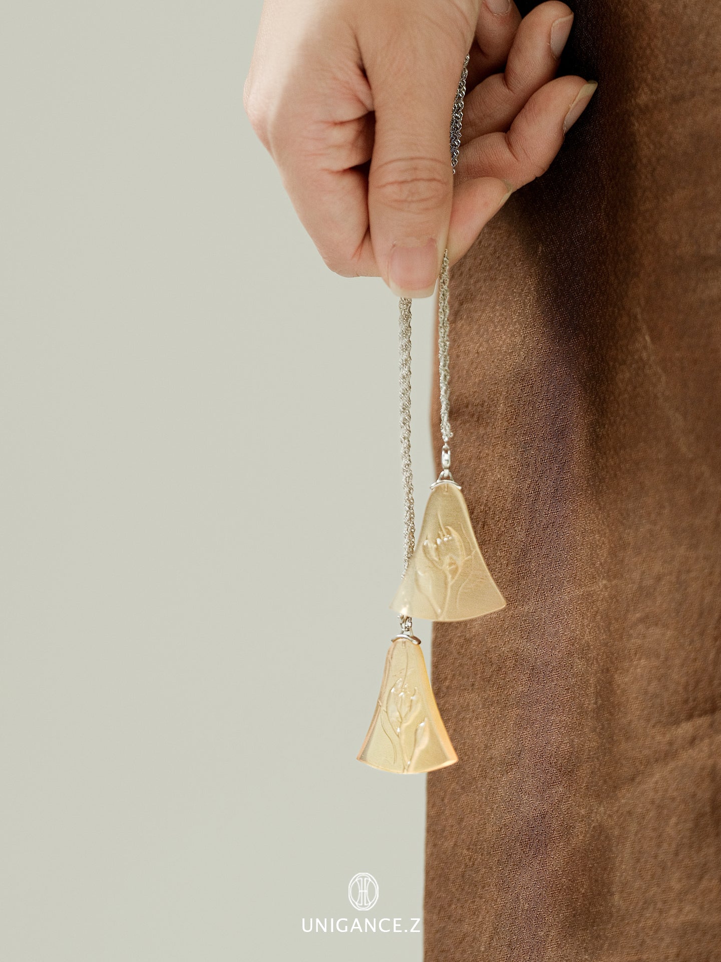 Gold bell-shaped pendant on a chain held by a hand against a neutral background