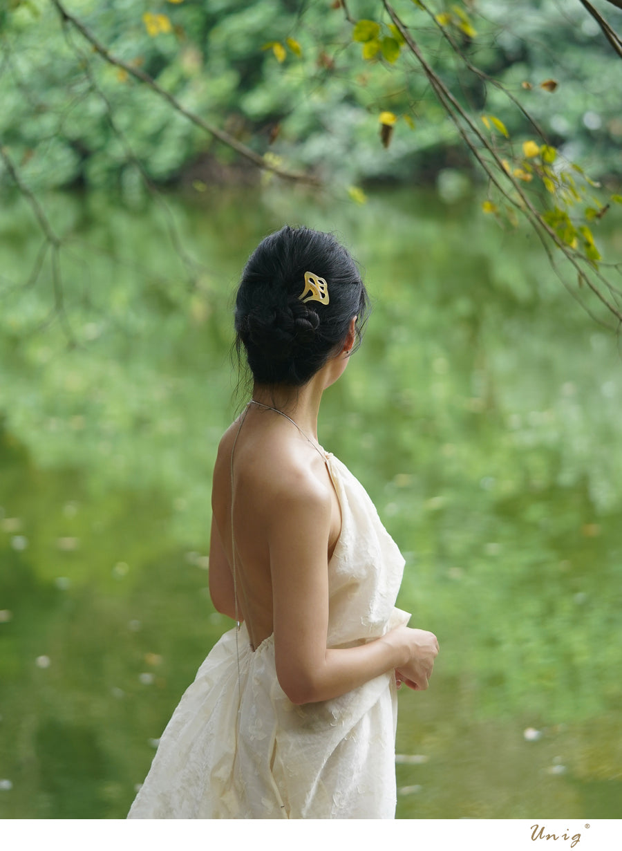 Woman in a white dress standing by a body of water with greenery in the background