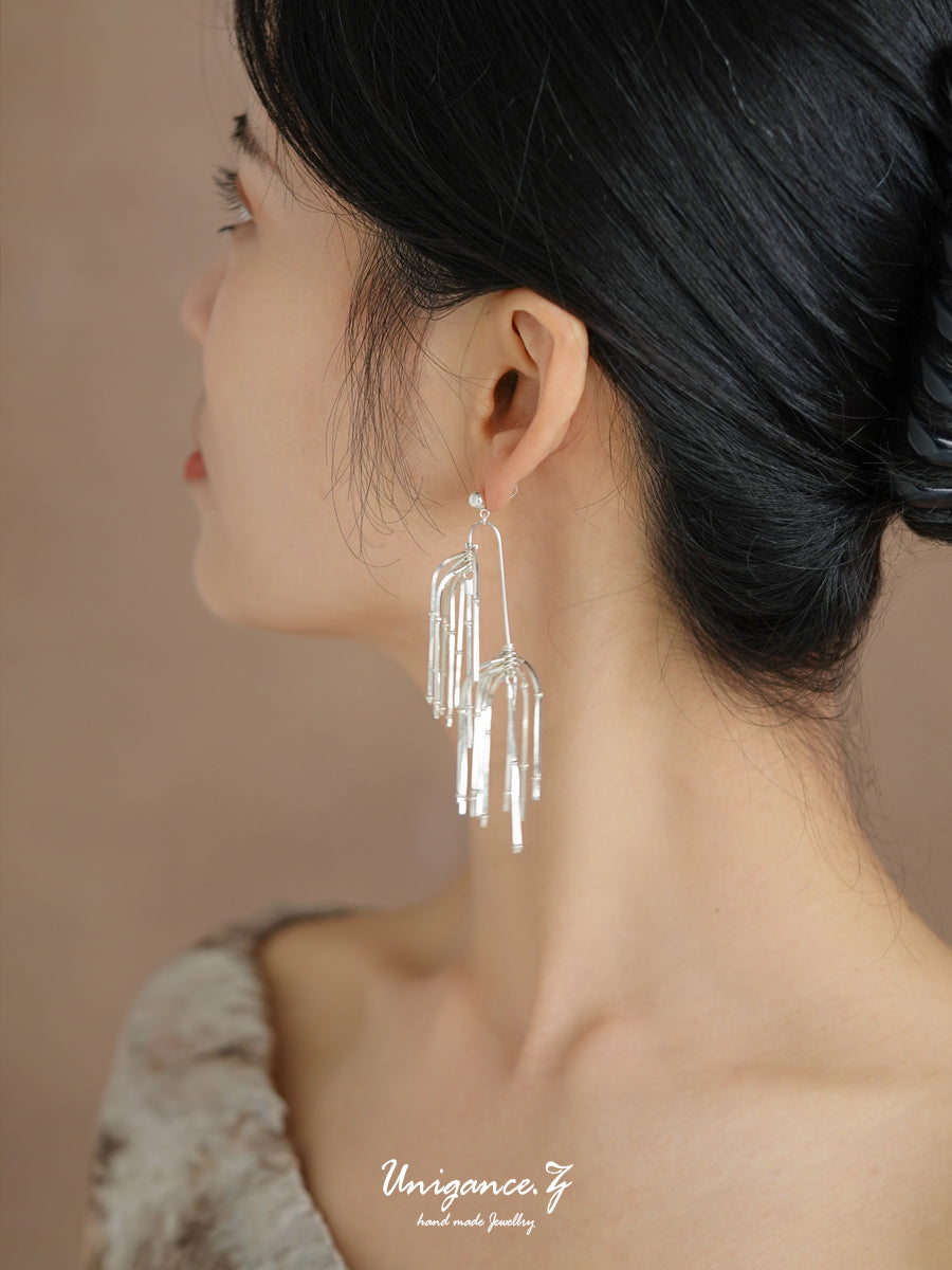 Woman wearing silver tassel earrings with a neutral background