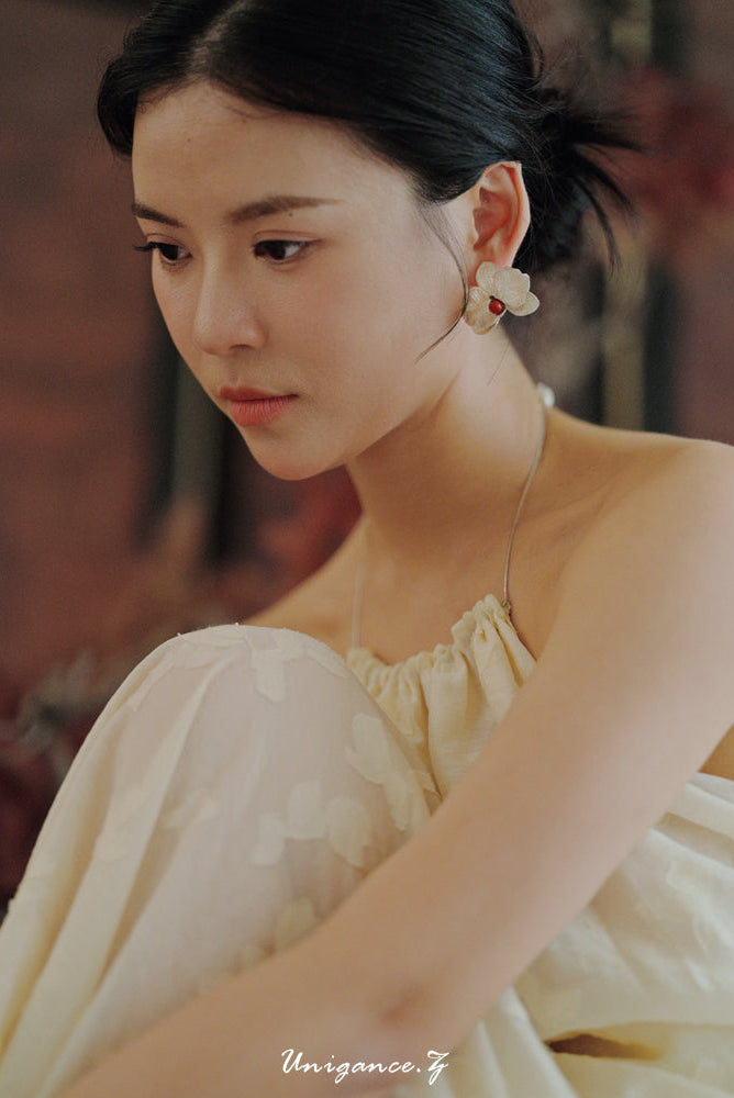 Woman in a light-colored dress with floral earrings, blurred background