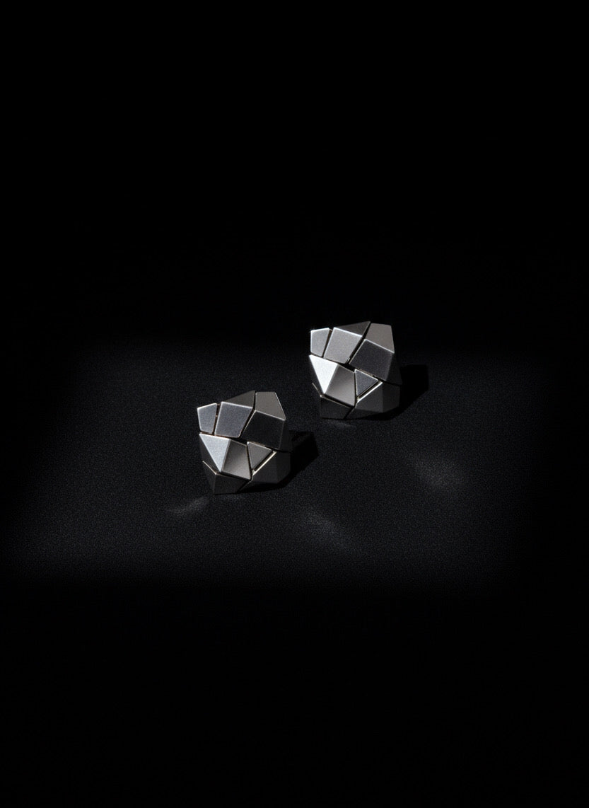 Two geometric silver earrings on a black background