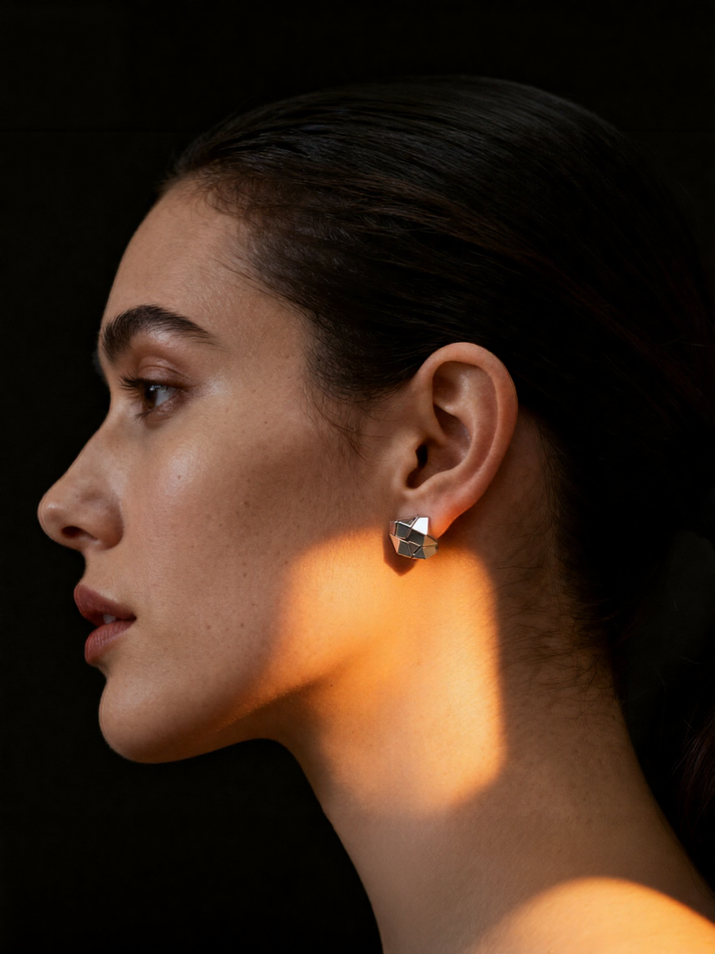 Cracks · Gold-plated Silver Earrings — Close-up of a woman's profile with a soft light on her face against a dark background