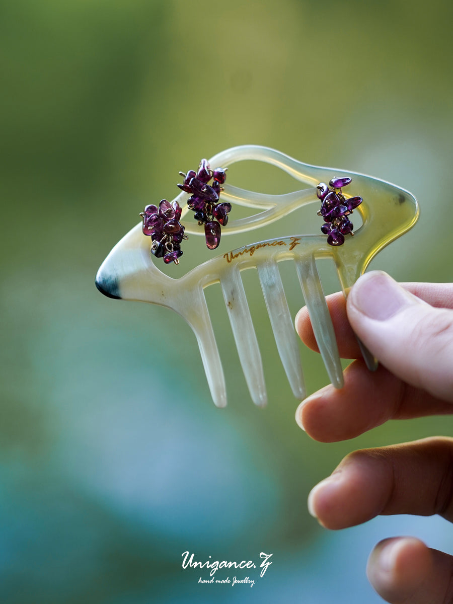 Crimson Bloom Branch Hair Comb — Clear hair comb with purple flowers held by a hand against a blurred green background