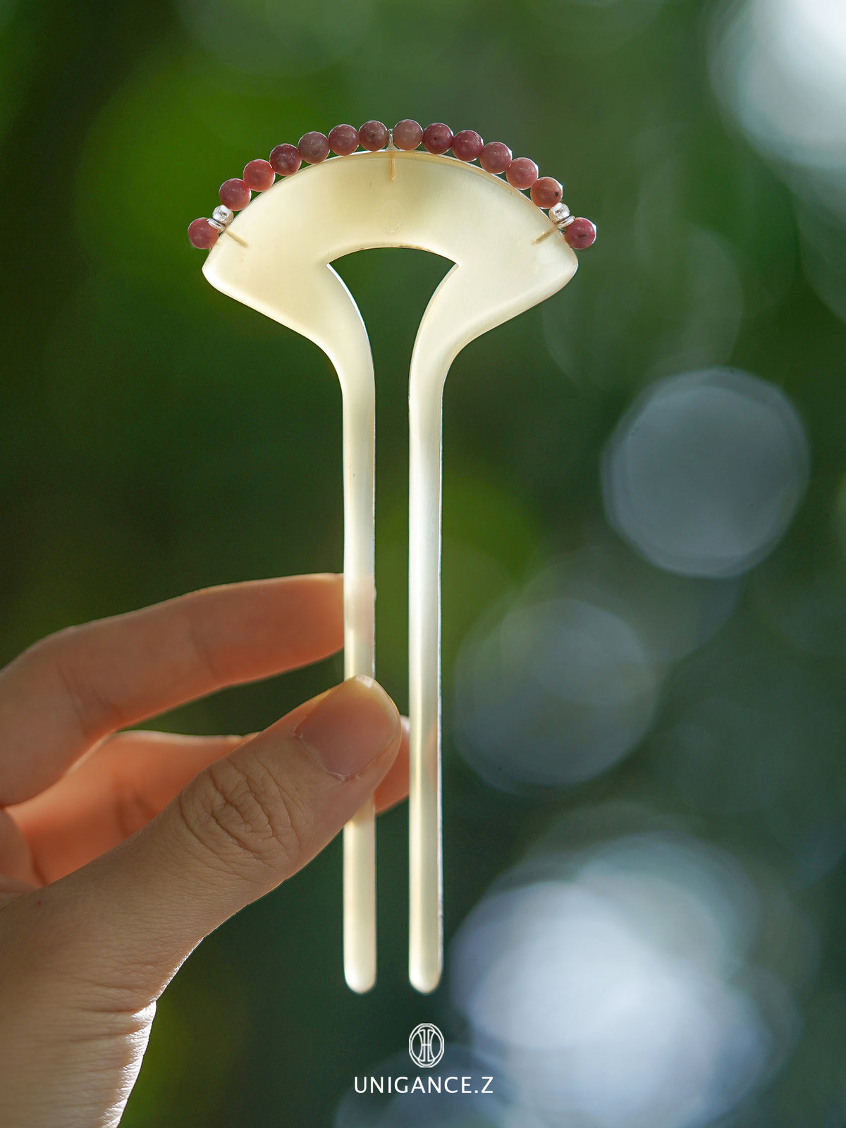 Crimson Touch Rhodonite Hairpin — Decorative hairpin with red beads held by a hand against a blurred green background