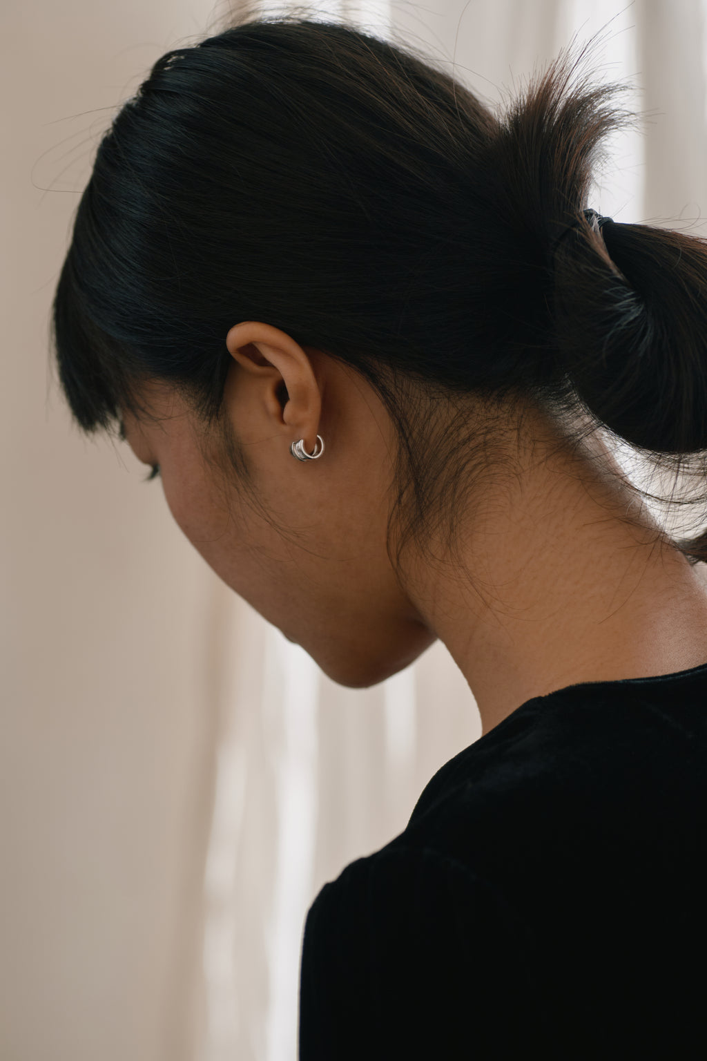 Double-Band Illusion Earrings — Person with black hair in a ponytail wearing a silver earring against a neutral background