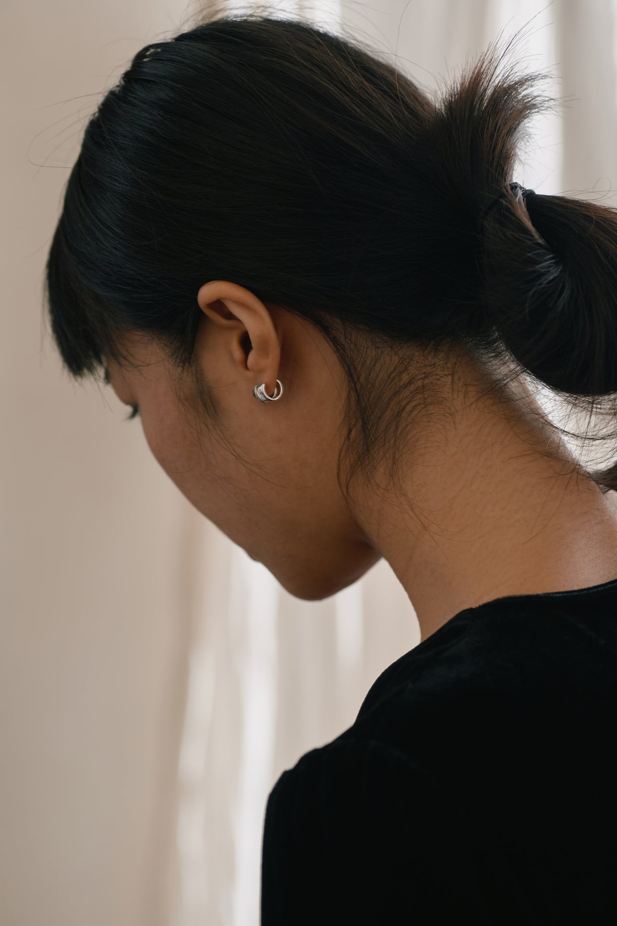 Double-Band Illusion Earrings — Person with black hair in a ponytail wearing a silver earring against a neutral background