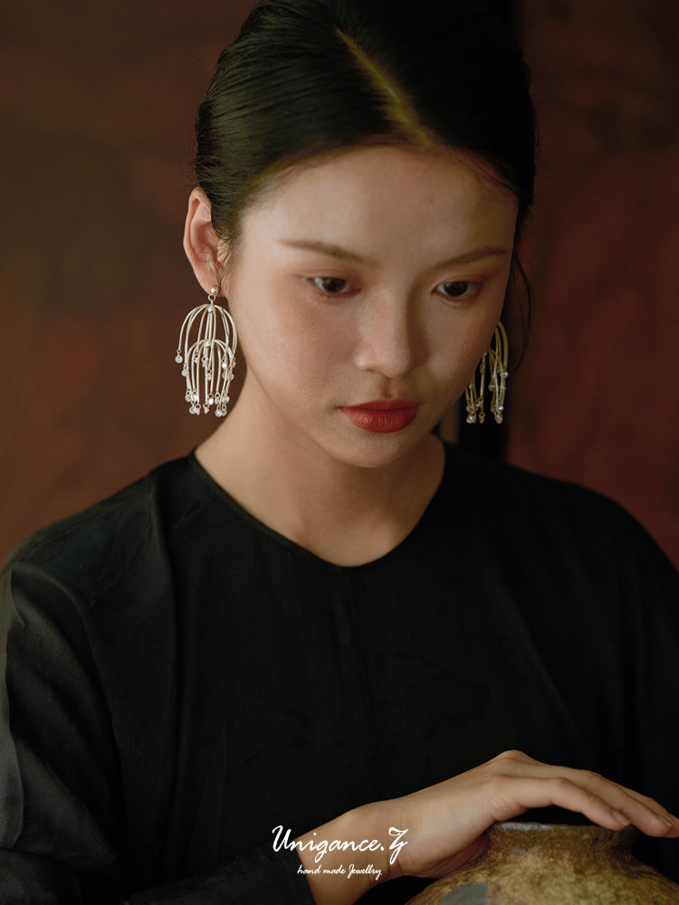 Drooping Begonia Drop Earrings — Woman wearing large earrings with a dark background