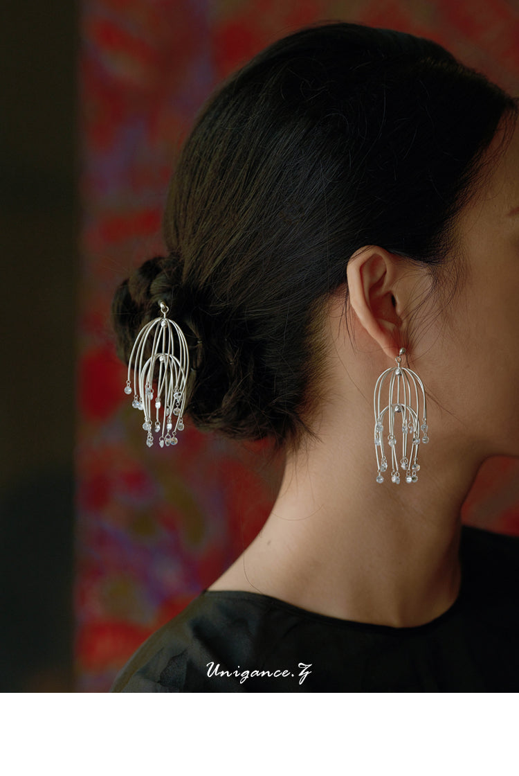 Drooping Begonia Drop Earrings — Close-up of a person wearing silver earrings with a blurred colorful background