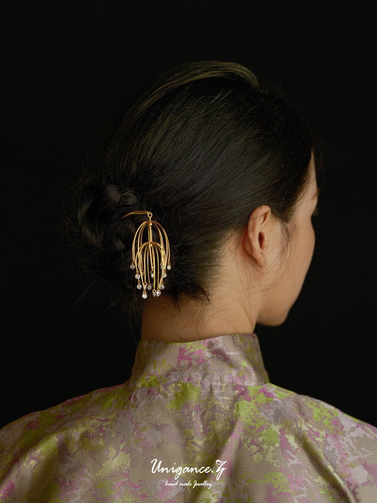 Person wearing a gold hair accessory with pearls against a dark background