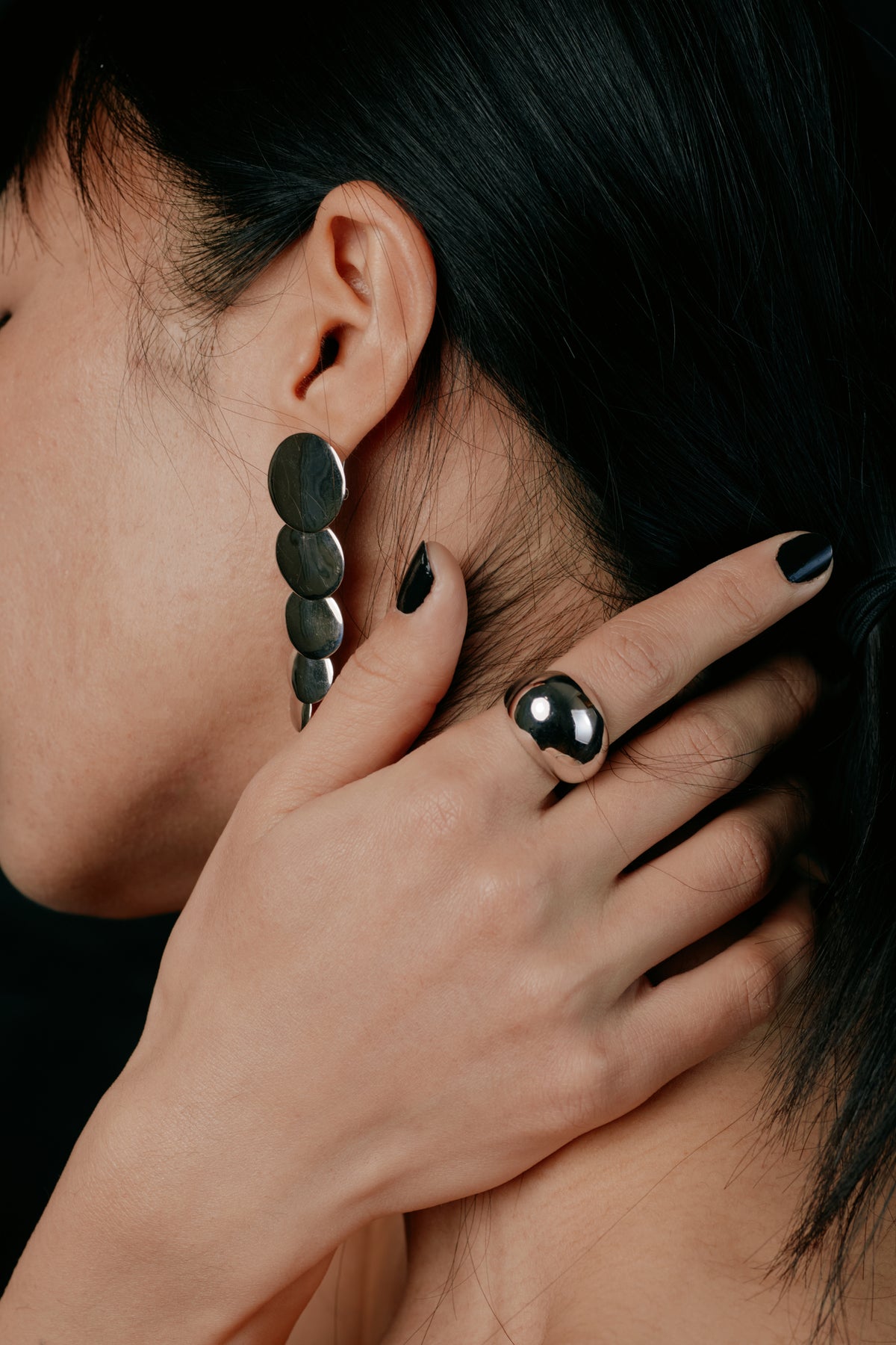 Egg Silhouette Silver Ring — Close-up of a person wearing black earrings and rings with a dark background