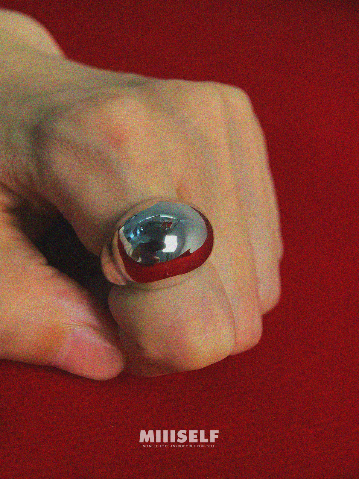 Egg Silhouette Silver Ring — Hand holding a small object with a red rim and blue center against a red background, featuring